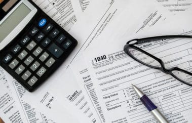 Tax forms spread out on table with calculator, pen, and eyeglasses