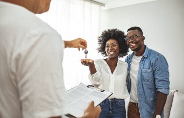 Handsome realtor is giving key to the new apartment to happy young couple.